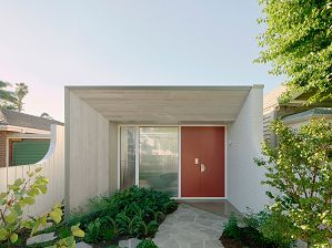 Red front door to single storey house with textured window, timber eave and crazy paving path