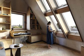 Photograph of attic showing the vaulted ceiling made of structural CLT coming almost down to meet the floor and a woman in the space looking out of the angled skylights.
