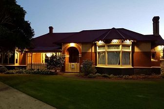 Dusk exterior of a single storey bluestone and redbrick homestead building with arched entry, whose design dates back to the mid-1840s.