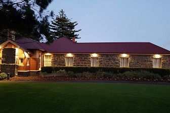 Dusk exterior of a single storey bluestone and redbrick homestead building showing a green lawn in the foreground.