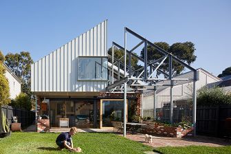View from the backyard with open trusses over the barbecue terrace and a boy playing with his dog in the yard,