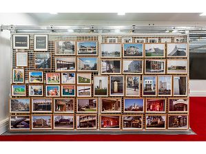Selection of framed colour photographs on display as part of the picture racks in the City of Melbourne's Art and Heritage Collection store. Photographs featured are by various artists and include street and cityscapes and portraits. Floor is covered in red carpet, walls are painted white and black blinds are behind the picture racks.