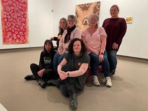 The group of artists from the Ngardang Girri Kalat Mimini (NGKM) collective are sitting in a gallery space smiling at the camera.