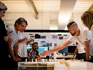 Seven people are gathered around a table looking at an architectural model.