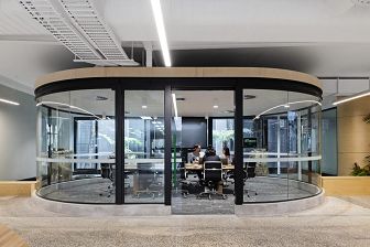 A team of three people hold a meeting at a long desk inside a glass oval-shaped room.