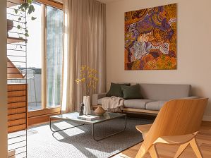 Photograph of a space with golden lighting, depicting a grey three-seater couch with green cushions and an Indigenous Australian artwork hung above