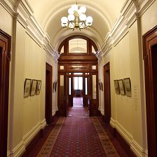 Corridor of the Old Treasury Building. The walls are cream, and the carpet burgundy. A line of framed images runs on either side of the corridor.