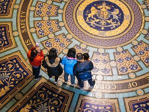(3) Photograph of a four adults and one child looking at a colourful titled floor