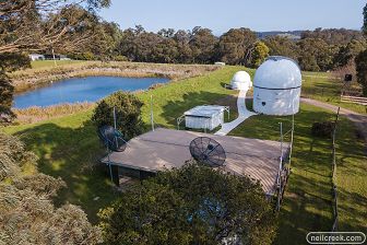 (1) Mount Burnett Observatory - aerial view, showing two observatory domes, metal shed, and log cabin, linked by concrete paths. Farmland and dam in background. (2) Monash Dome, Celestron Dome and shed, with Milky Way overhead. (3) Monash Dome illuminated by the Moon overhead, and red lights on the side. (4) Eighteen inch telescope inside Monash Dome, viewed from behind while it is pointed at the night sky. (5) Monash Dome and Celestron Dome in daylight, linked by concrete path. (6) Monash Dome at night with image of stars projected onto the exterior walls and roof. Door and telescope slit are open showing interior lights.