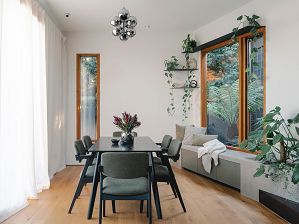 A dining room with timber floors, white walls and ceiling, a reading-nook to the right and an integrated planter