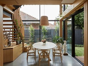 A dining table in a fully-glazed double-height room, with stair in background and a feature wicker light pendant