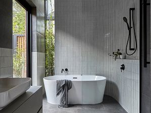 An image of a free-standing white bath in front of a narrow window looking to greenery in a light-filled bathroom