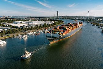 An aerial of shot of a ship being towed by a tugboat with the West Gate Bridge in the background.