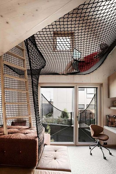 Photo of a double-storey kids bedroom with the upper part being half mezzanine half void covered by a cargo netPhoto from the outside looking at the fully glazed ground floor with the metal clad upstairs gable above.