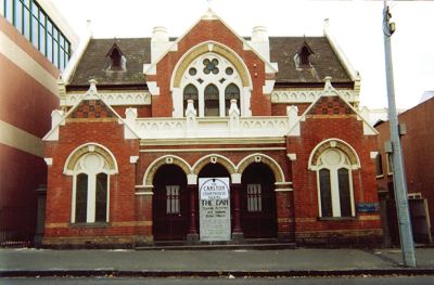 Front view of a Victorian Gothic-style brown brick facade with contrast cream-coloured detailing.