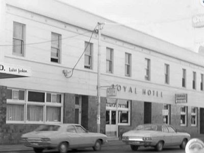 Black and white photograph of Barkly St view of the outside of the Royal Hotel. Two story building facade with sign reading Royal Hotel and two cars parked in front.