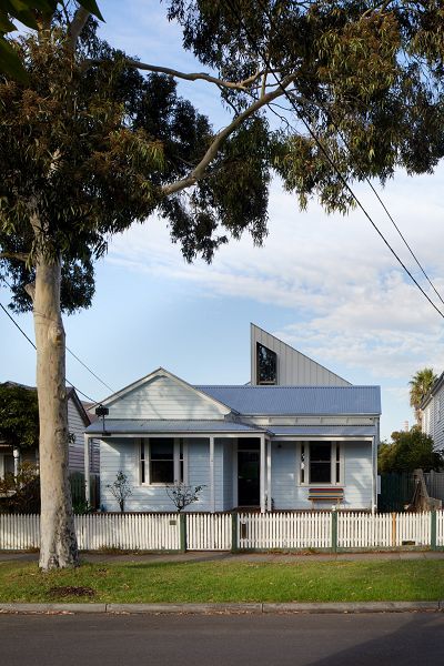 View of house from the street with only a triangle of new roof visible.