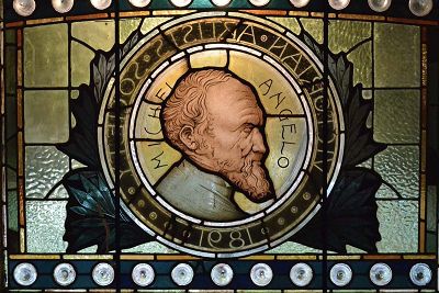 Photograph of a stained glass window with a circular design and a side profile of Michael Angelo.