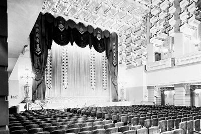 An early 20th century black and white photograph of the interior of a theatre with ornate curtains concealing the screen.