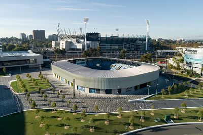 An aerial view of Melbourne Park showing Kia Arena with a glimpse of its iconic blue seating inside and extensive open areas with newly planed Eucalyptus trees