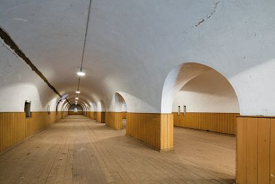 Empty cavernous interior of magazine, buildings length divided by archways with a white ceiling and wooden floors.