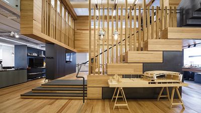 A very light-filled side view of the studio staircase, with several vertical timber elements reaching from the stairs to ceiling, with a table in front with an architectural model placed on it.