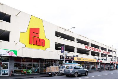 Exterior of a multi-storey market with a large yellow sign with initials FM decorating the front. Cars drive by on the street.