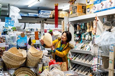 A woman wearing a yellow jacket examines a sticky rice steamer in a kitchen appliance store.