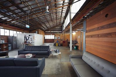 Interior colour photograph of an open plan space furnished with sofas. The walls are timber clad, a rug is on the concrete floor, the timber structure of the roof is exposed.