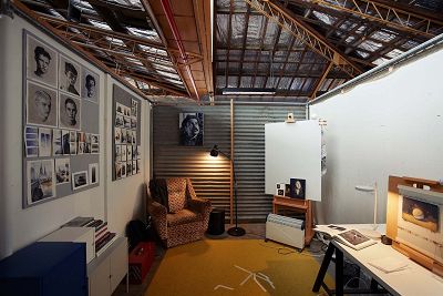 Interior colour photograph of a studio space. The back wall is corrugated iron and the roof's timber structure is exposed. A sitting chair sits in one corner.