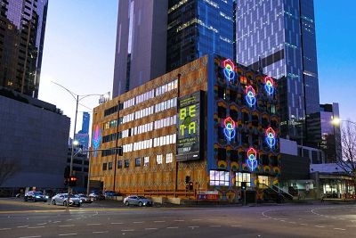 A colour photograph of a corner building painted in bright colours with digital screens illuminated brightly coloured lights.