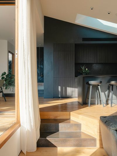An image of a kitchen and living room with angled ceiling, black kitchen and timber floors with steps