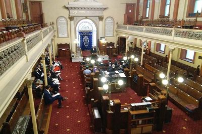 Judges and solicitors seated in ground floor on wooden benches with grill-worke surrounding mezzanine seating of women's gallery.