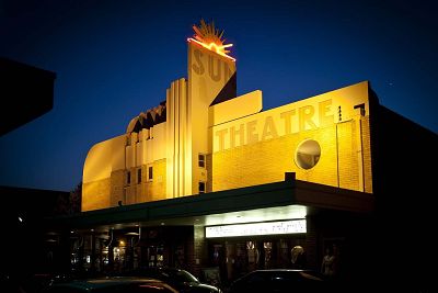 Exterior photo of an art deco style theatre building built in 1938. The photo is taken at dusk, with the facade lit up and the words Sun Theatre clearly visible.