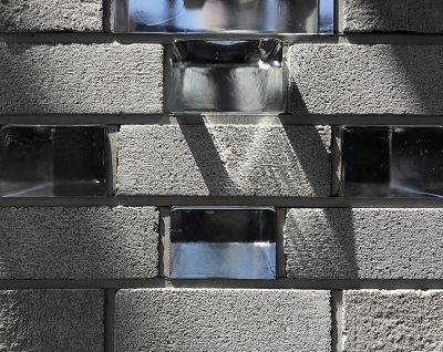 close up of bricks in the facade of the museum. Grey bricks alternate with glass bricks, with sunlight shining through the glass.