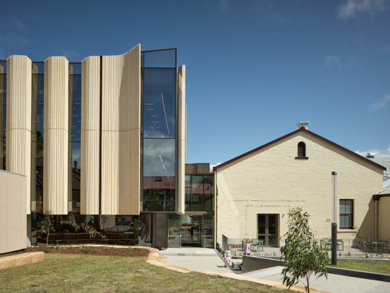 Front elevation showing multi-storey renovation at left juxtaposed with smaller scale white-painted brick gable-roof building at right.